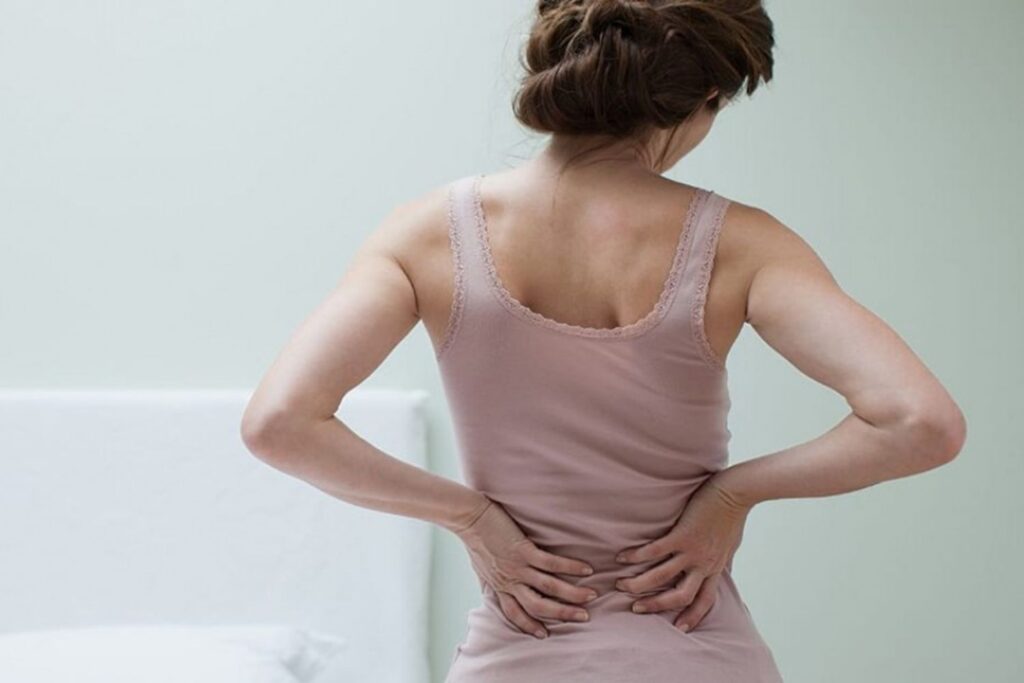Frau hält sich mit den Händen den Rücken. Man sieht sie nur von Hinten.